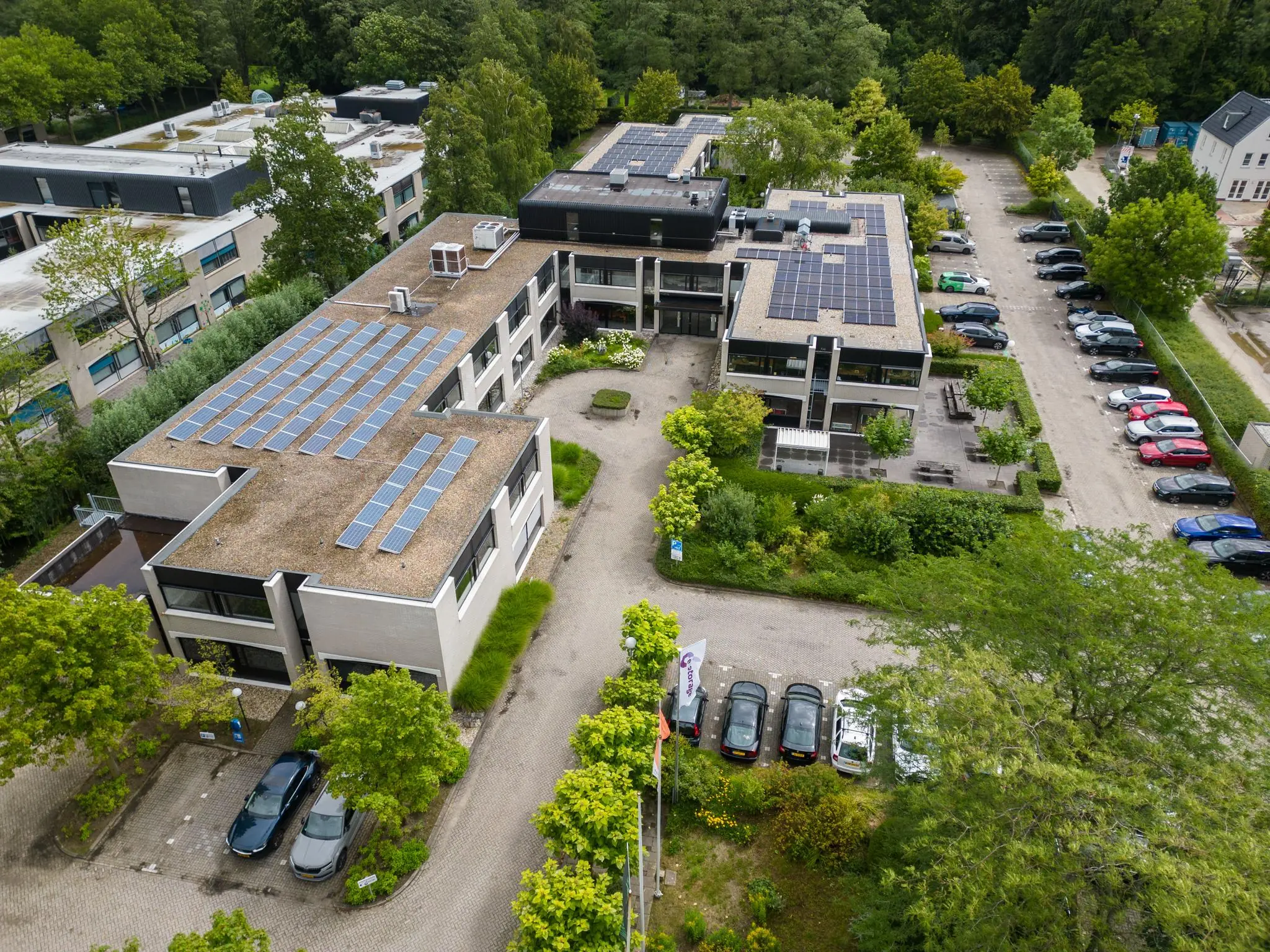 Luchtfoto van het gebouw aan de Burgemeester Verderlaan met zonnepanelen op het dak en omringende parkeerplaatsen.